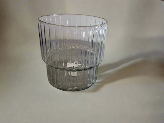 Clear glass ribbed vase with a pedestal on a textured background