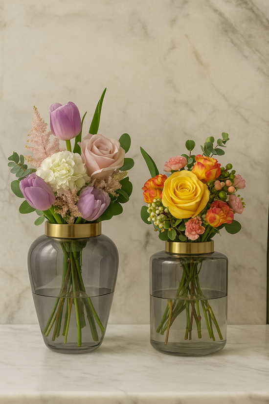 Two floral arrangements in ombre vases with gold bases on a marble surface.
