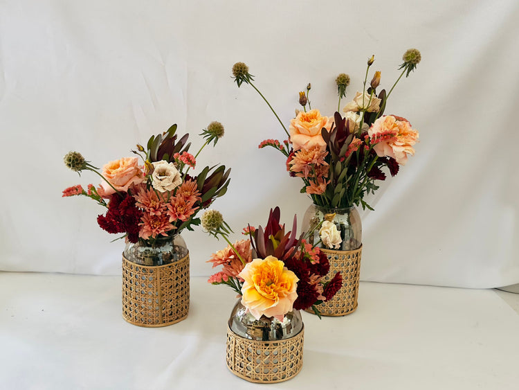 Three floral arrangements in wicker vases on a white background