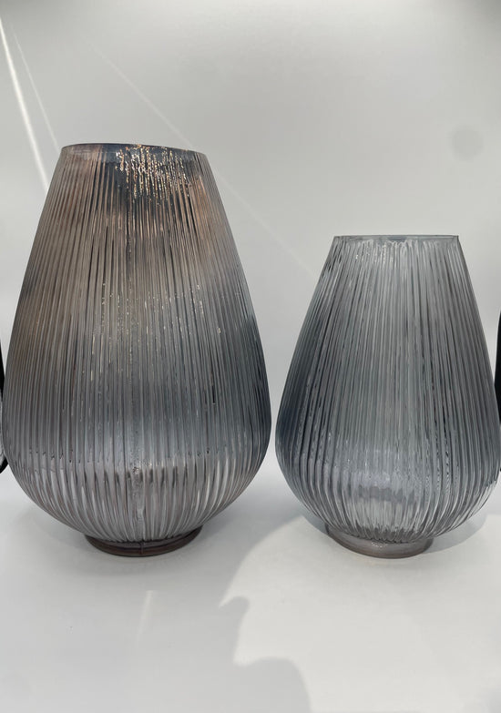 Two ribbed glass vases on a white surface with a light gray background