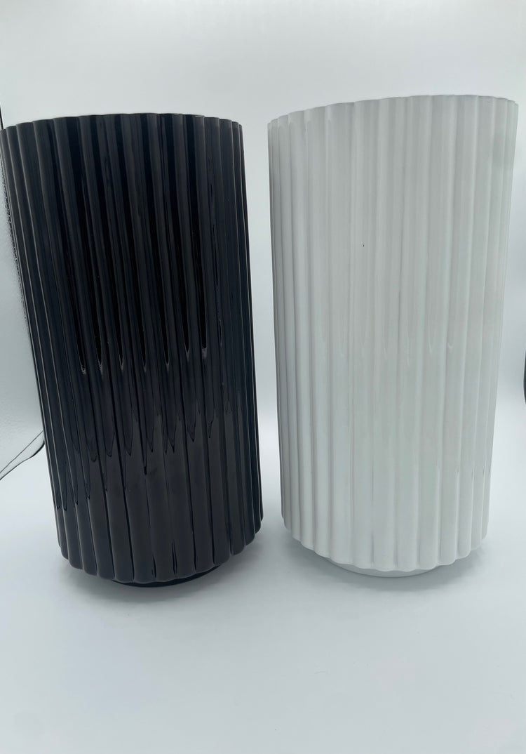 Two cylindrical vases, one black and one white, with ribbed texture on a white background.