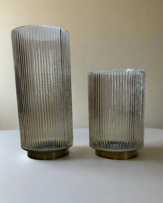 Two ribbed glass vases on a textured surface with a light blue wall background.