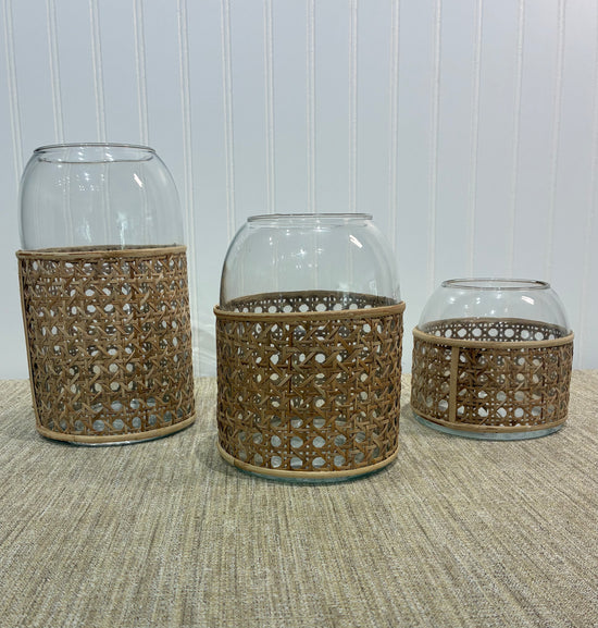 Three clear glass vases with raffia on a textured surface with a white paneled wall background.