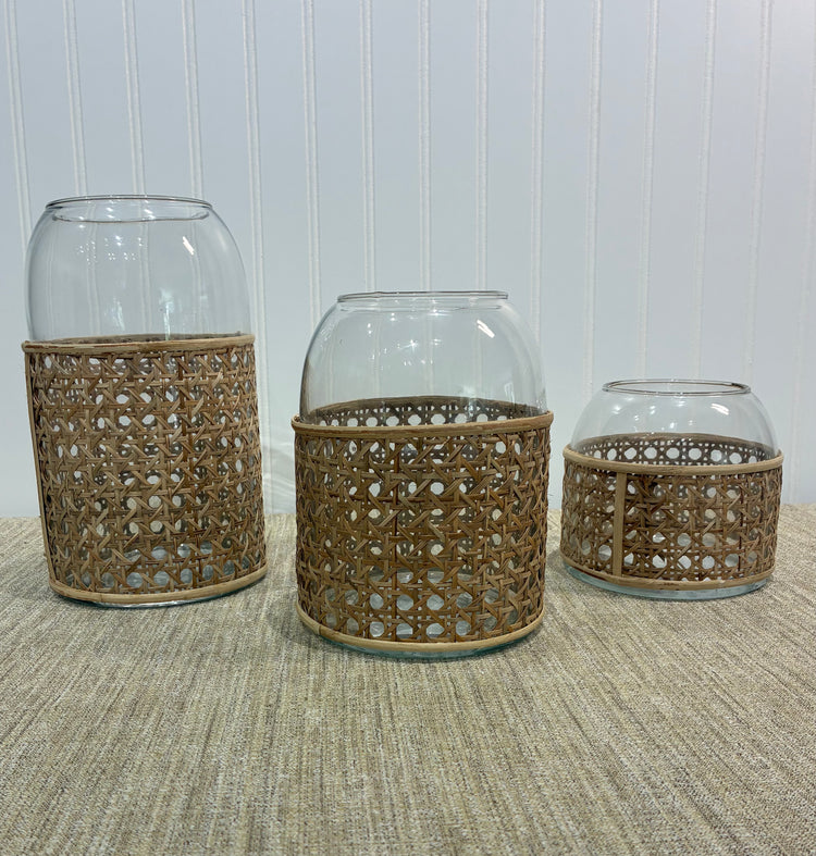 Three clear glass vases with raffia on a textured surface with a white paneled wall background.