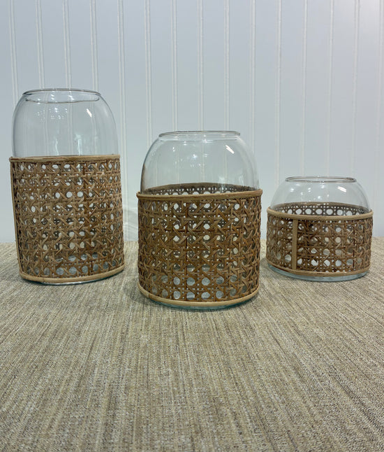 Three glass vase with woven rattan covers on a textured surface.