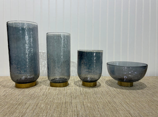 Four smoky glass vases of different shapes on a textured surface with a light background
