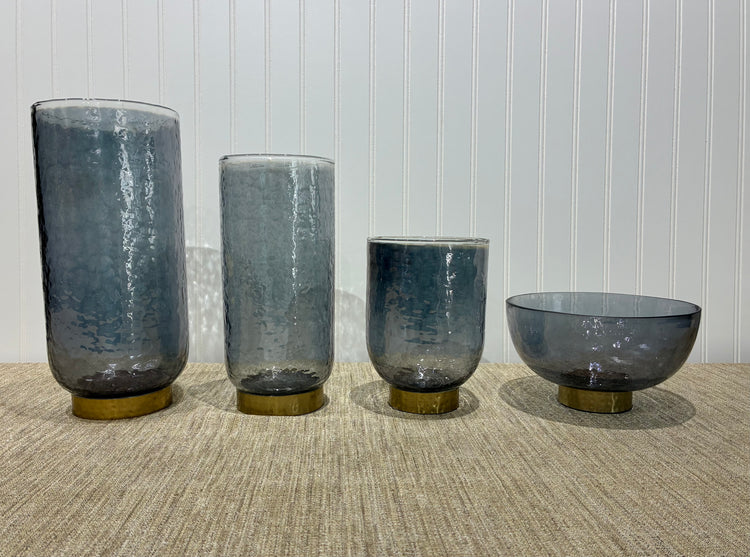 Four smoky glass vases of different shapes on a textured surface with a light background