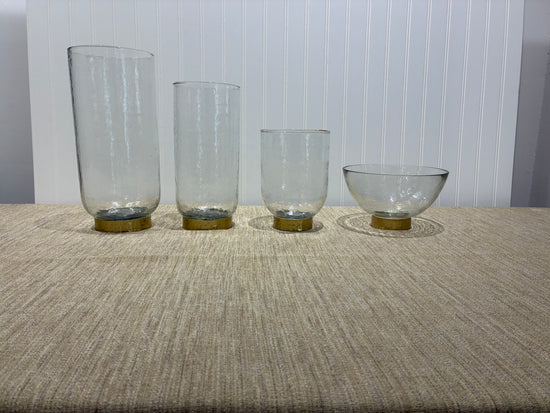 Four clear glass vases with metallic bases on a textured surface.