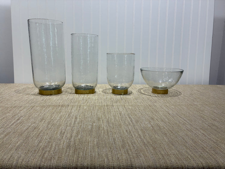 Four clear glass vases with metallic bases on a textured surface.