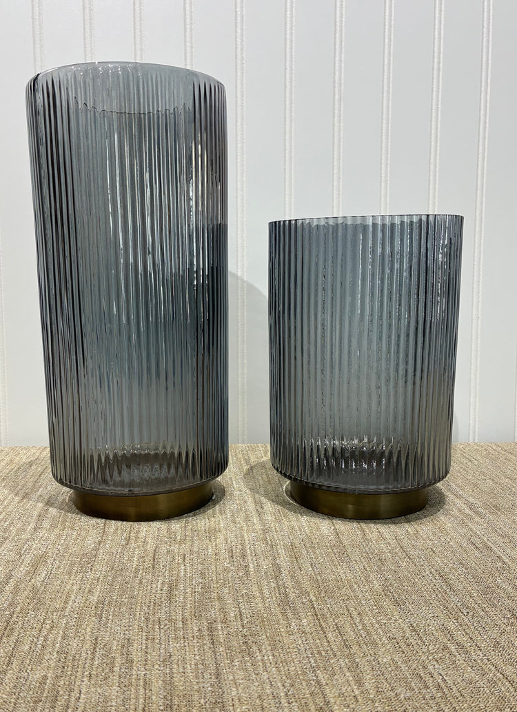 Two Smoked ribbed glass vases on a textured surface with a white paneled wall background.