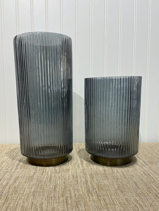 Two ribbed smoke glass vases on a textured surface with a neutral background