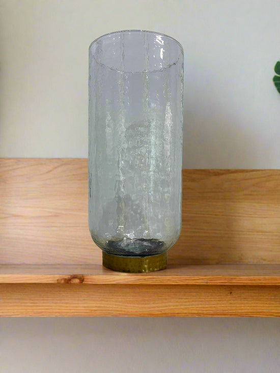 Clear glass vase with a gold cap on a textured surface