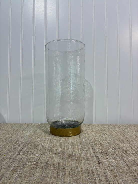 Clear glass vase with brass cap on a textured wall