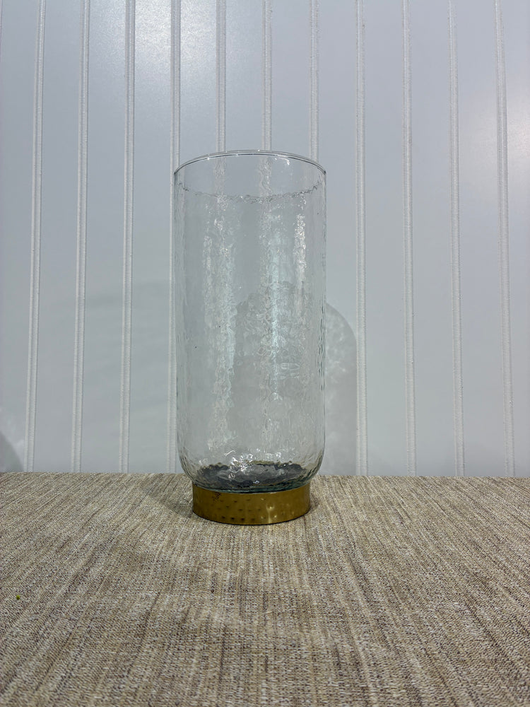 Clear glass vase with brass cap on a textured wall