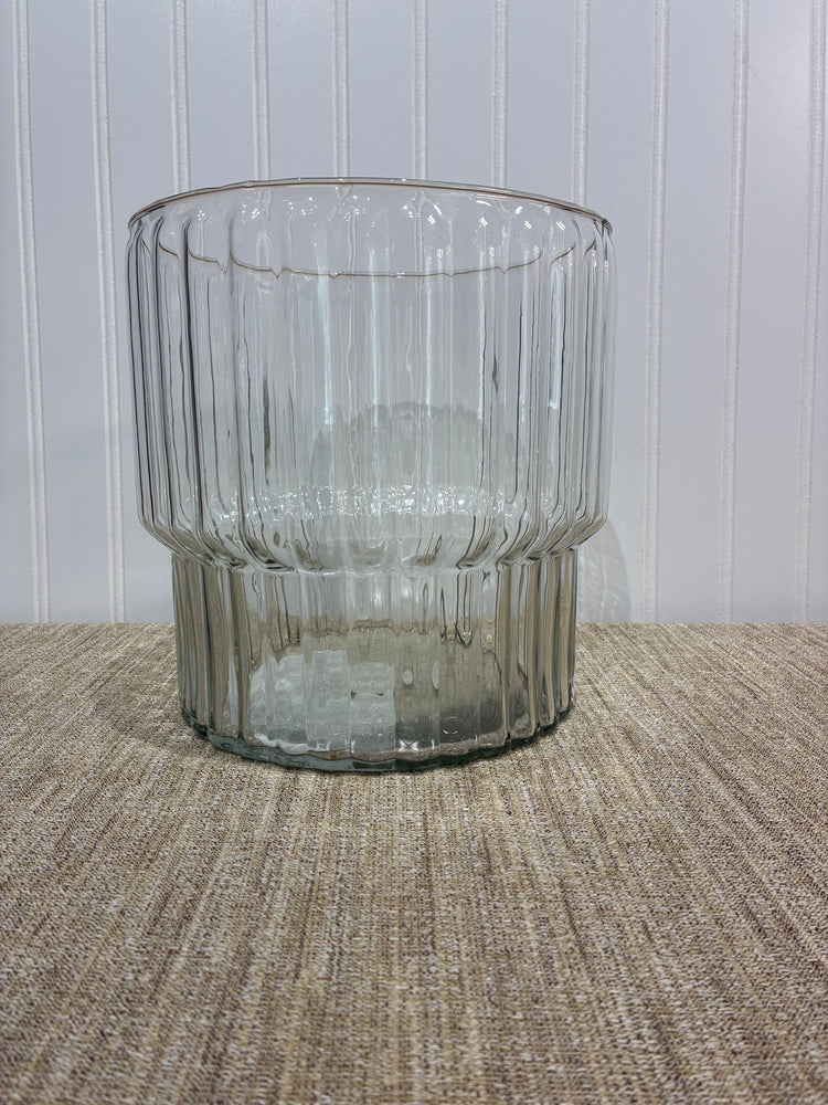 large Clear ribbed glass vase on a textured surface with a neutral background