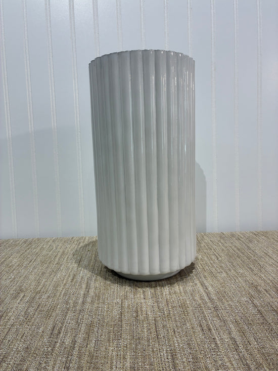 Tall white ribbed vase on a textured surface with a white background