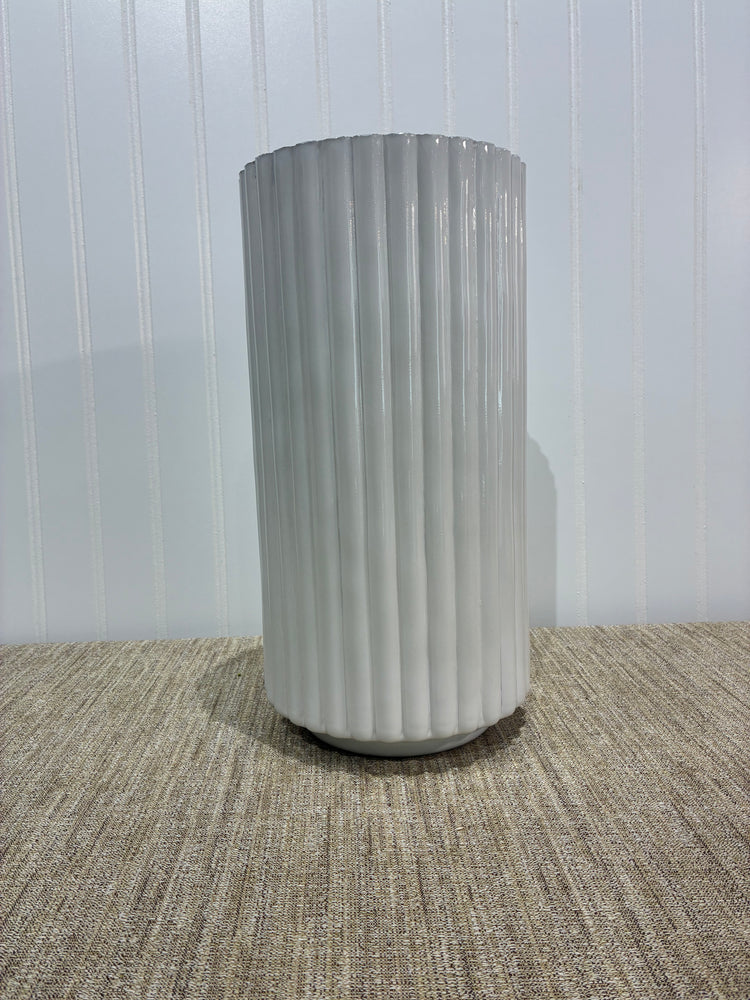 Tall white ribbed vase on a textured surface with a white background