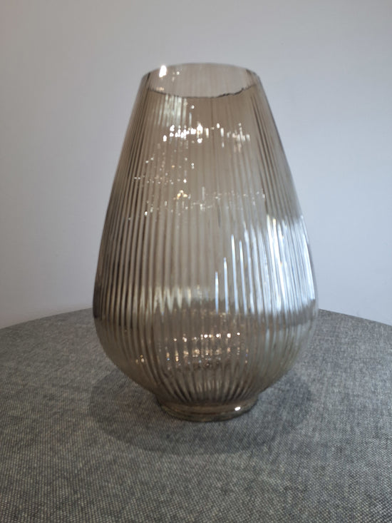 beige ribbed glass vase on a gray textured surface.