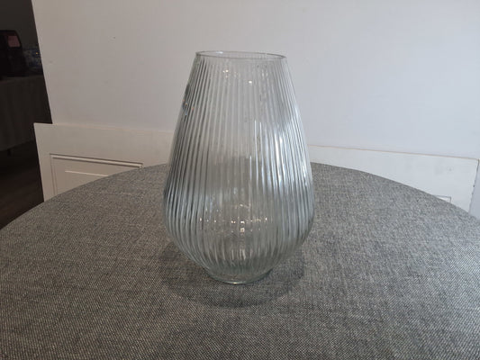 Clear ribbed glass vase on a gray textured surface.