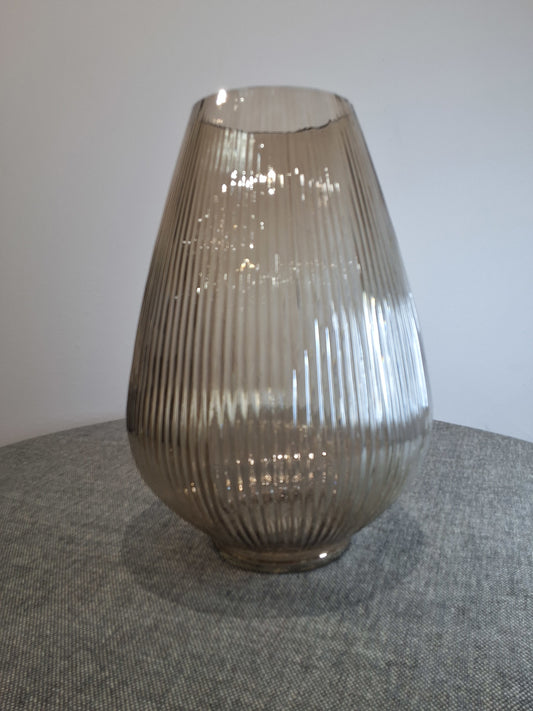 beige ribbed glass vase on a gray textured surface.